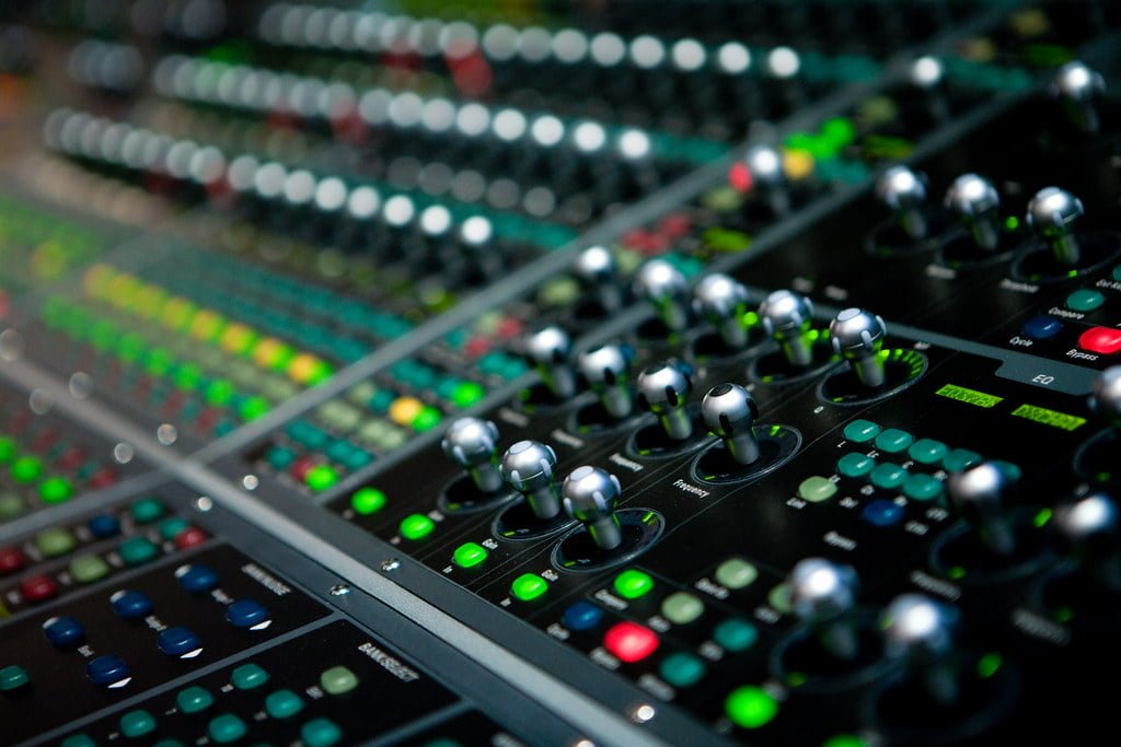 Close-up of an audio mixing console with knobs, sliders, and buttons, showcasing a shallow depth of field.