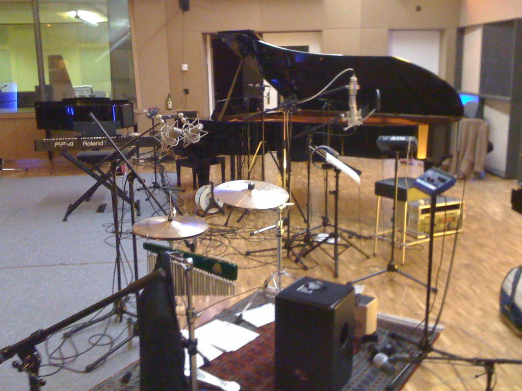 Music studio with a grand piano, drum set, electric keyboard, various microphones, and audio equipment.