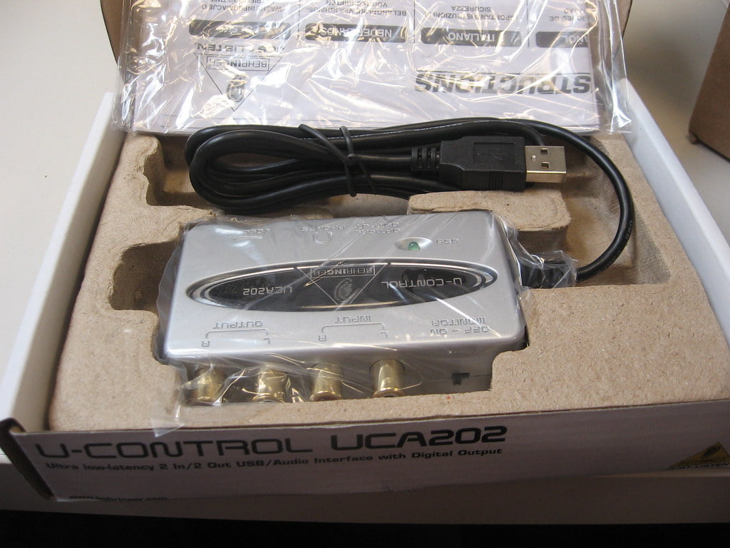 A U-CONTROL UCA202 audio interface with a digital output is packaged in its original box, partially covered by a plastic bag. A USB cable is coiled beside the device.