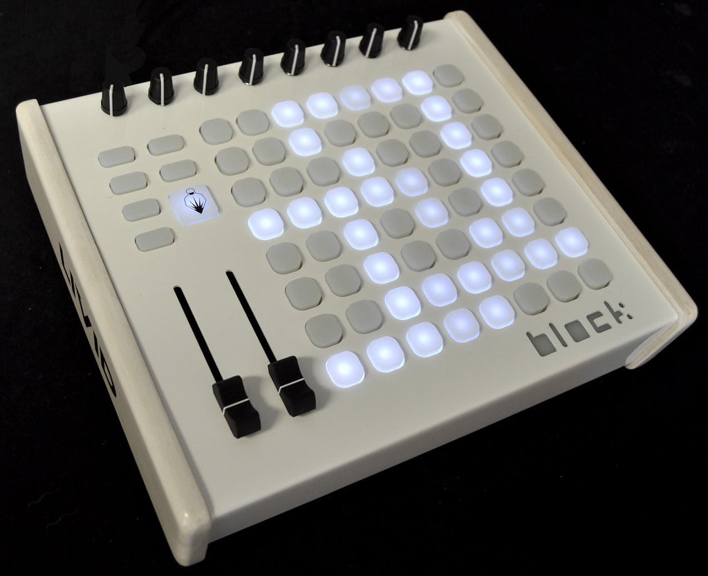 A lit-up MIDI controller with a grid of illuminated pads, two vertical sliders on the left, and a logo above the grid.