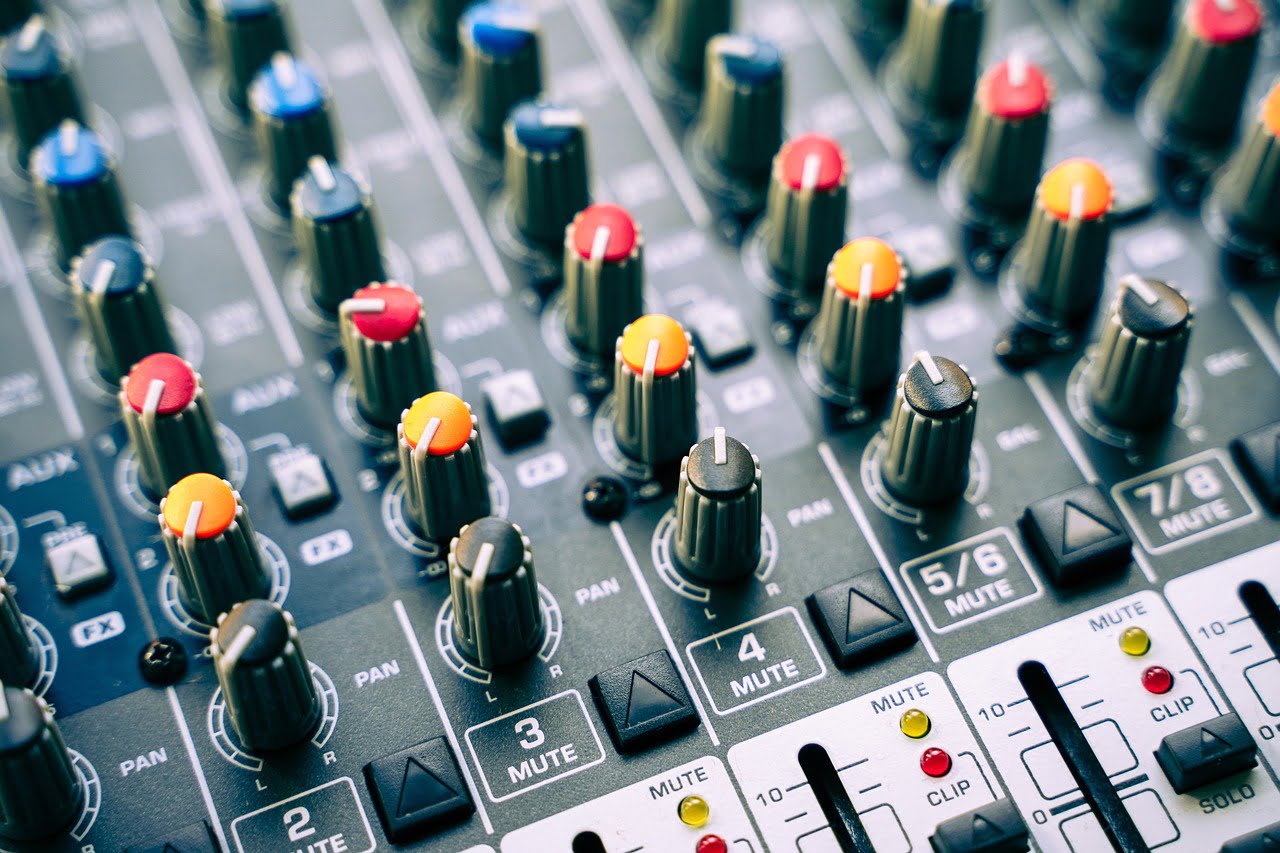 Close-up of a sound mixing console with various knobs and sliders for adjusting audio levels, some labeled with functions such as PAN, MUTE, and FX.