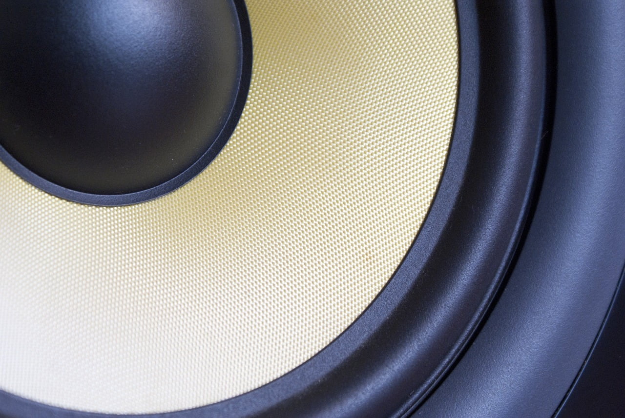 Close-up of a speaker cone with a black surround, showcasing its textured yellowish central diaphragm and dust cap.