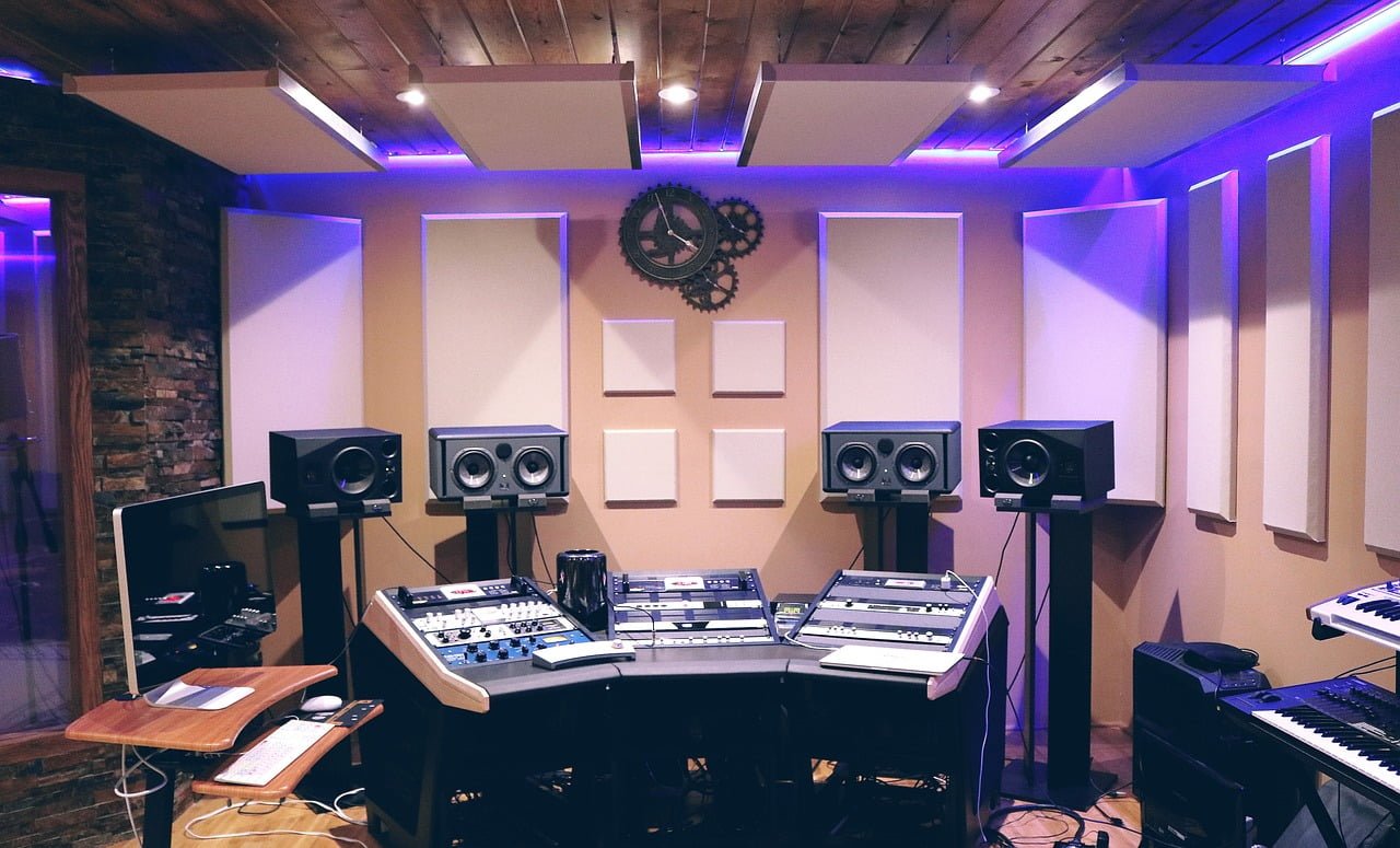 A modern music studio with sound mixing equipment, studio monitors, and synthesizers, highlighted by ambient purple lighting, against a backdrop of acoustic panels and a decorative gear wall clock.