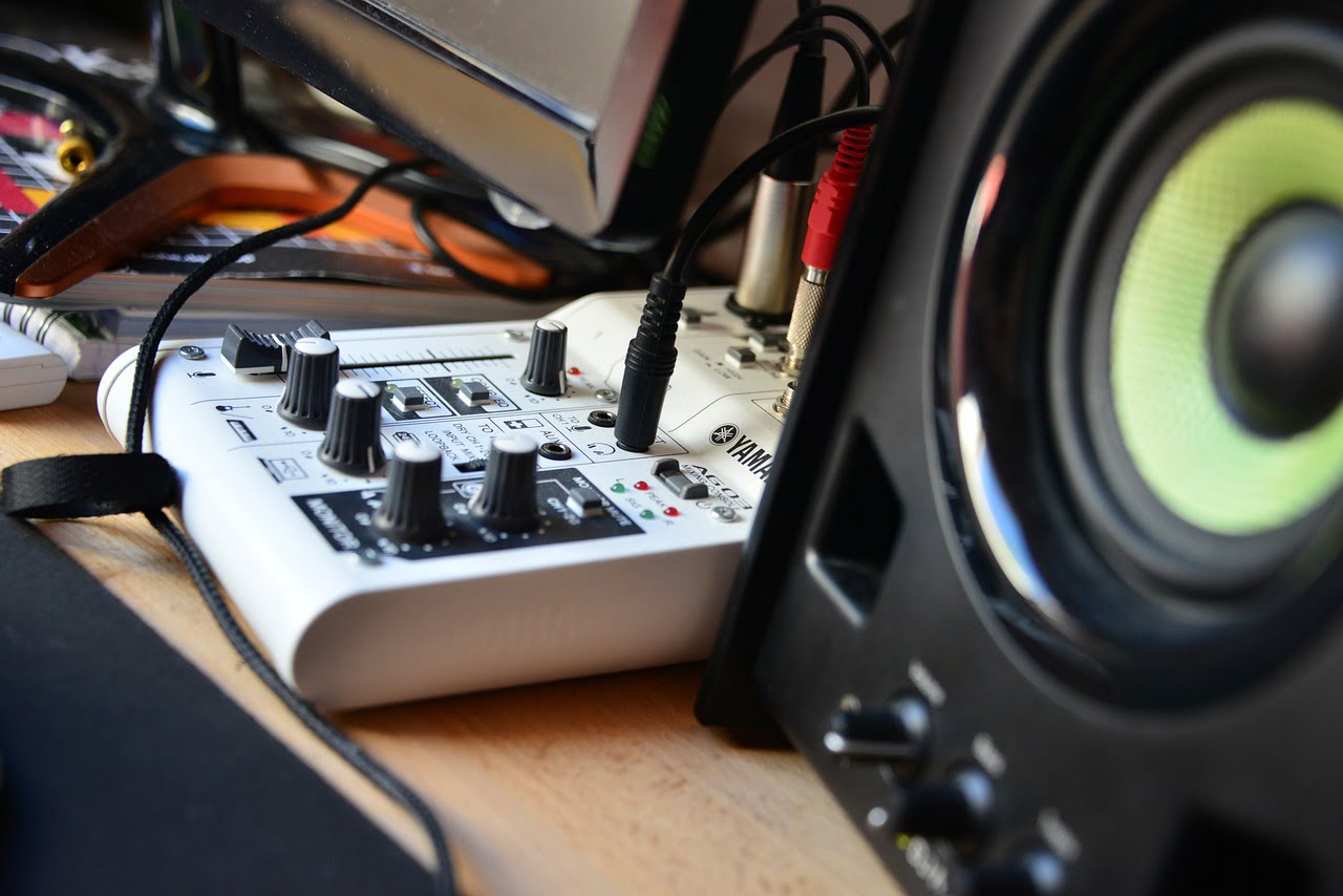 Close-up of an audio mixing console connected to a speaker on a cluttered desk with various cables.