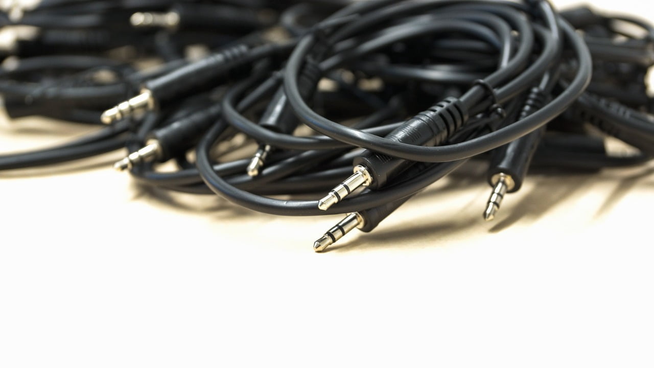 A heap of black 3.5mm audio cables with male connectors on a light background.