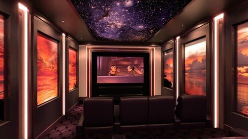 A home theater room with black seats and ambient lighting, displaying an animated movie on the screen, surrounded by wall art depicting landscapes, and a ceiling that resembles a starry night sky.