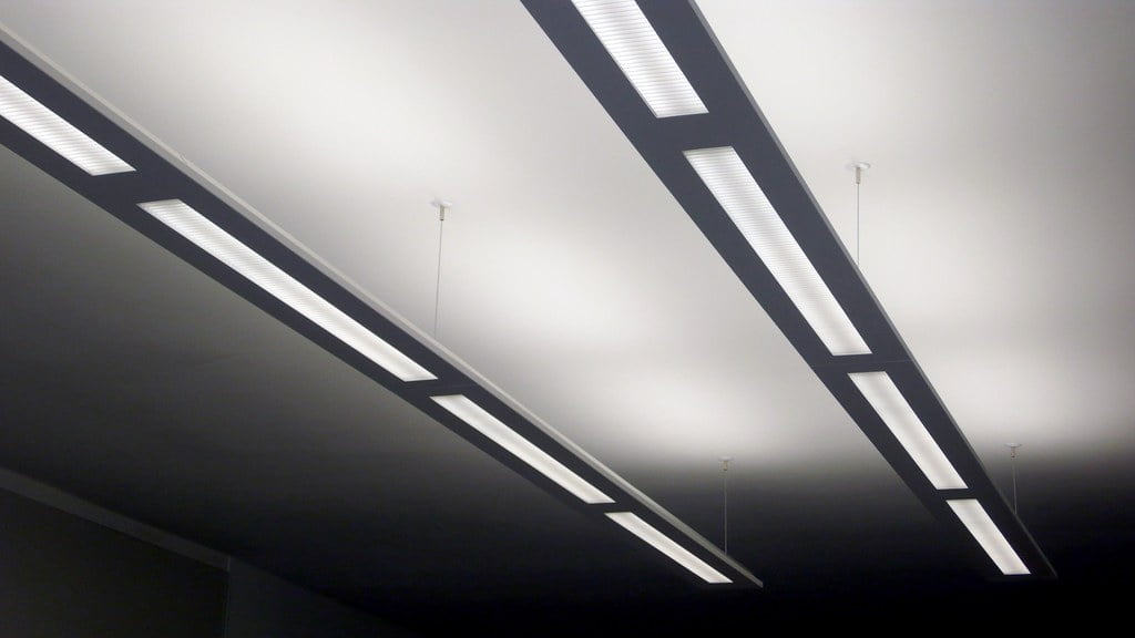 A modern interior with a dark ceiling featuring a series of long, rectangular, and angular light fixtures emitting a bright white light.