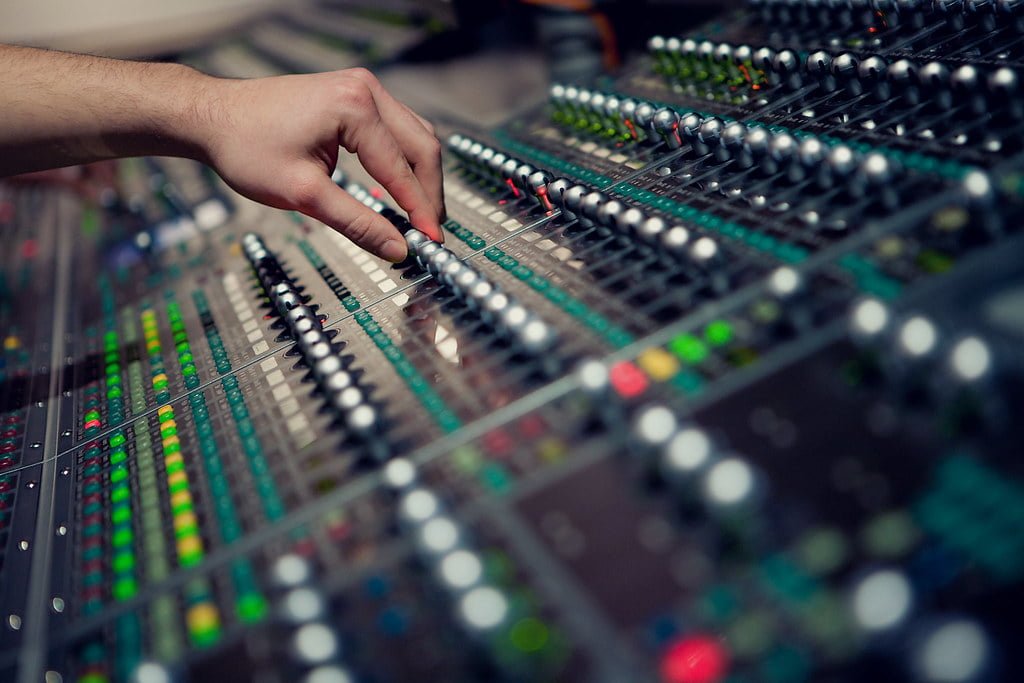 A person's hand adjusting knobs on a professional audio mixing console with many buttons and sliders.