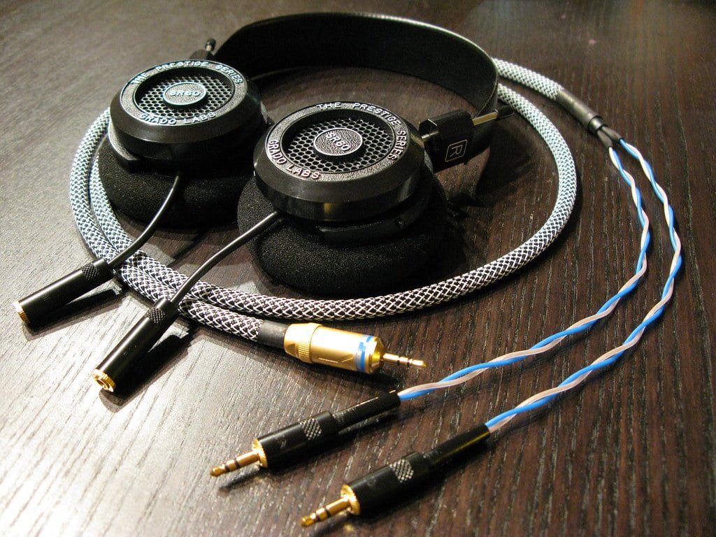 A pair of black over-ear headphones with details labeling "Prestige Series" and "Grado Labs" on a wooden surface, featuring a braided cable with a 3.5mm jack and a gold-plated adapter.