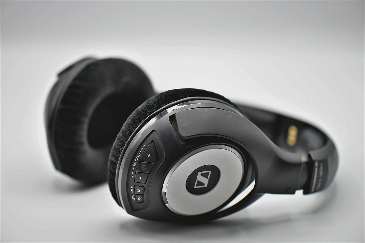 A close-up of a pair of over-ear headphones with black ear cushions and a control panel on the left earcup, set against a white background.