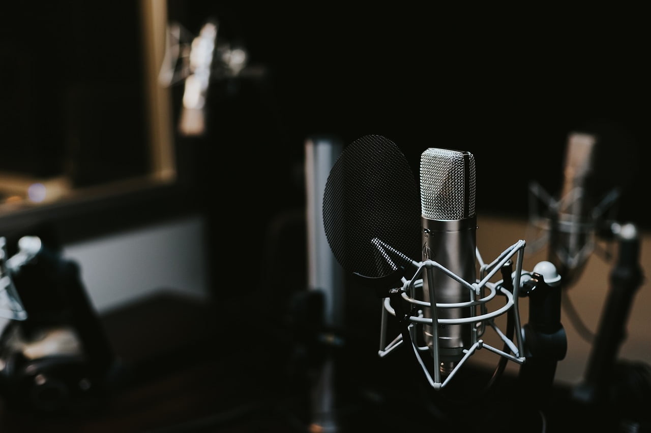 Two professional microphones with pop filters set up in a dark studio environment.