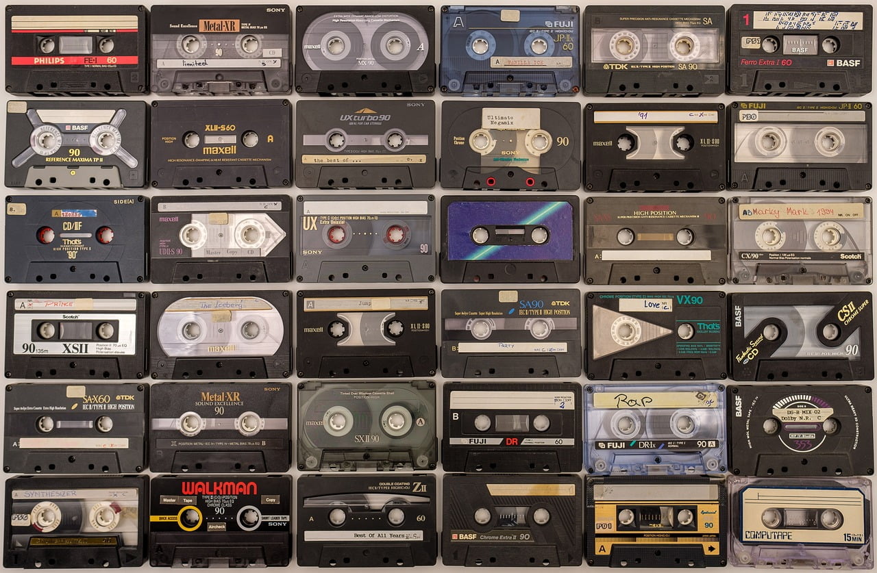 A collection of various brands and types of cassette tapes, some labeled with handwritten notes, organized in rows against a flat surface.