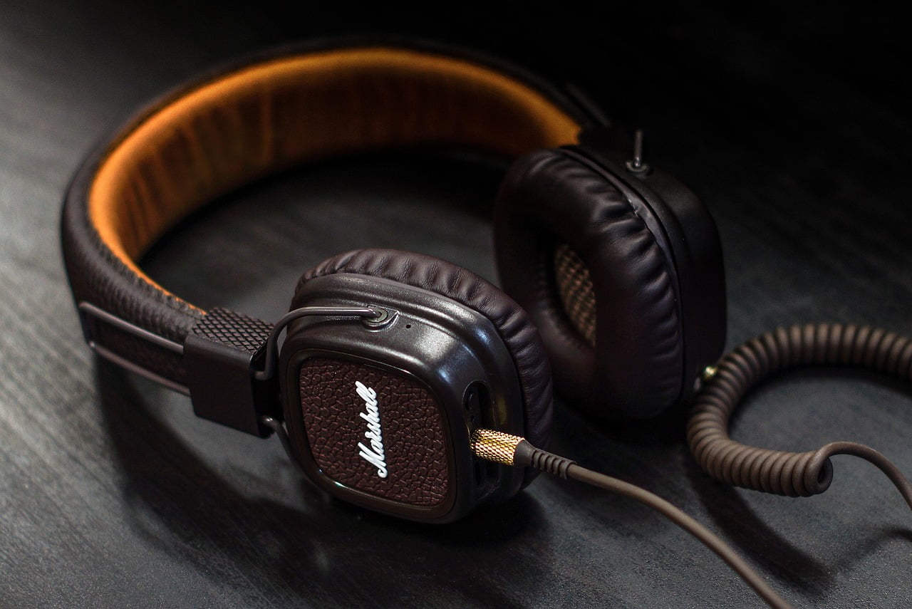 A pair of brown Marshall headphones with a coiled cable on a dark textured background.