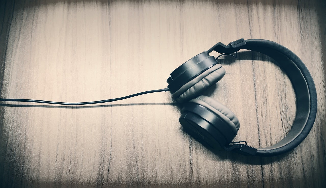 Black over-ear headphones with a cable lying on a wooden surface, depicted in a monochromatic tone.