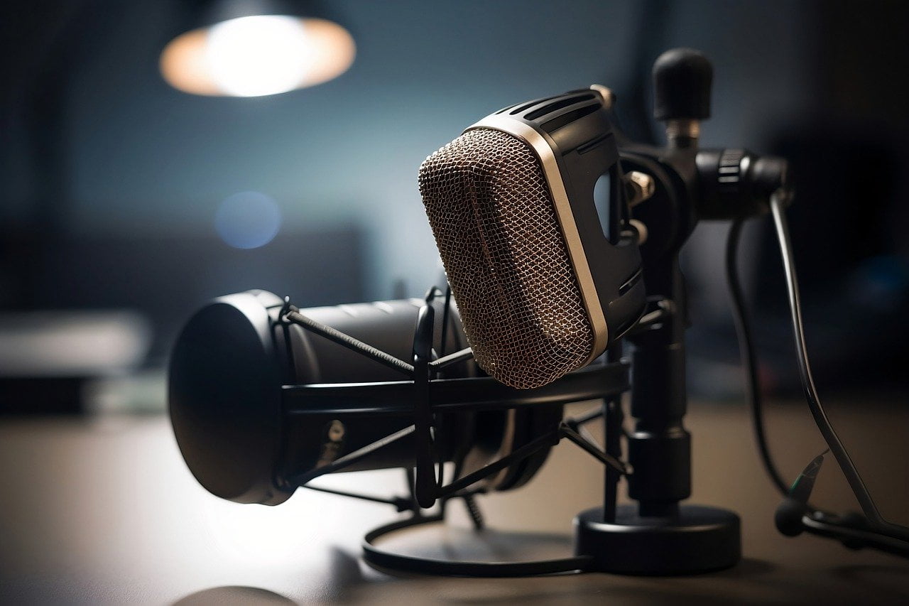 A professional microphone with a pop filter and shock mount set up in a studio environment, with a blurry background featuring soft lighting.