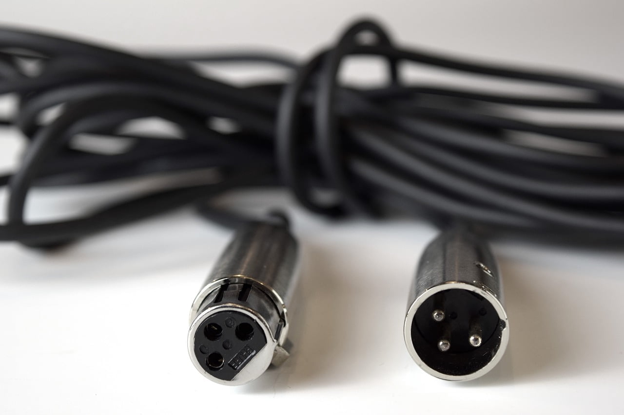 Two XLR audio cables with male connectors in focus, coiled and resting on a white surface.