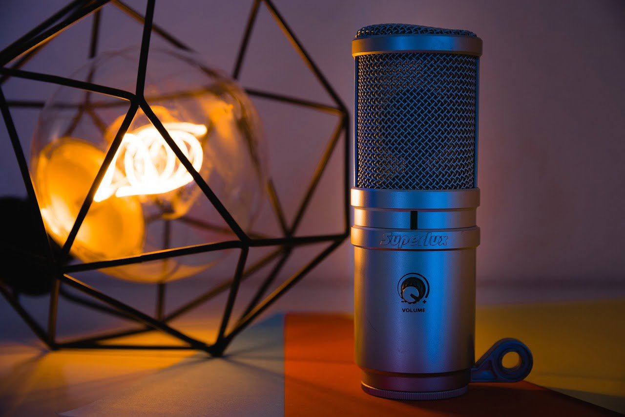 A Superlux condenser microphone with a metallic finish stands on a table, illuminated by warm ambient lighting, with a geometric wireframe lamp in the background.