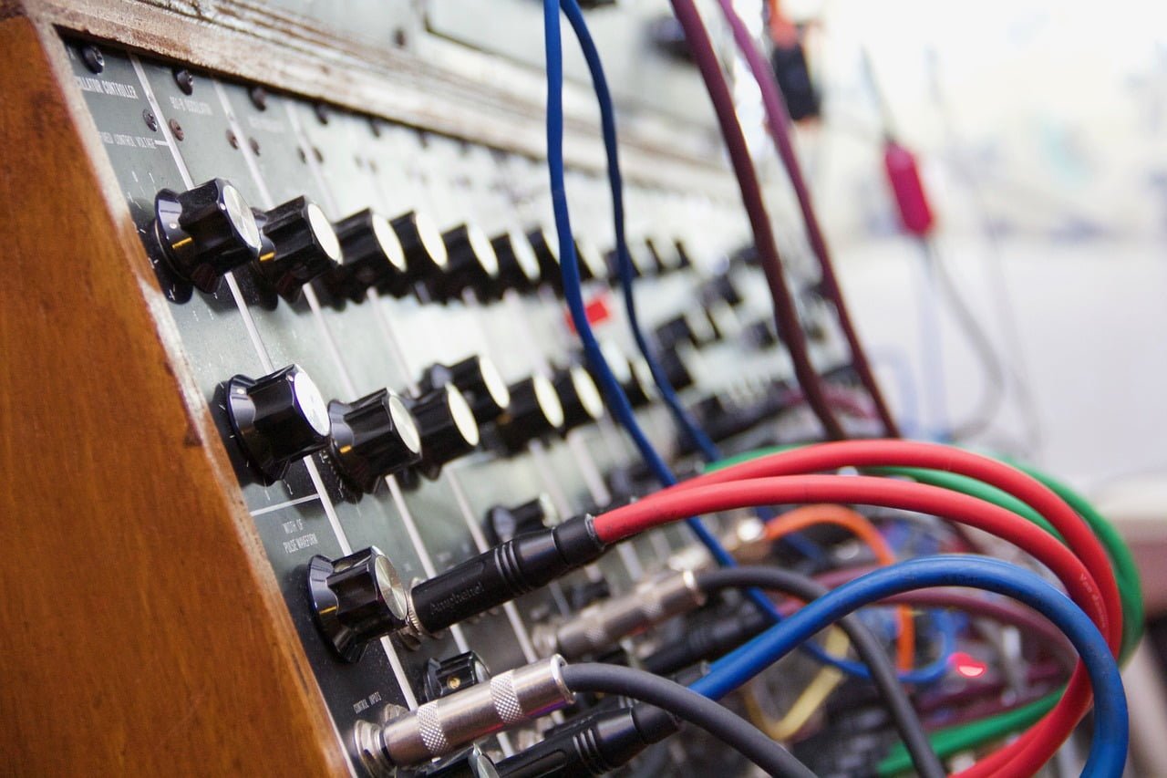 A close-up of a vintage audio mixer's panel with knobs and several plugged-in audio cables in blue, red, and black.