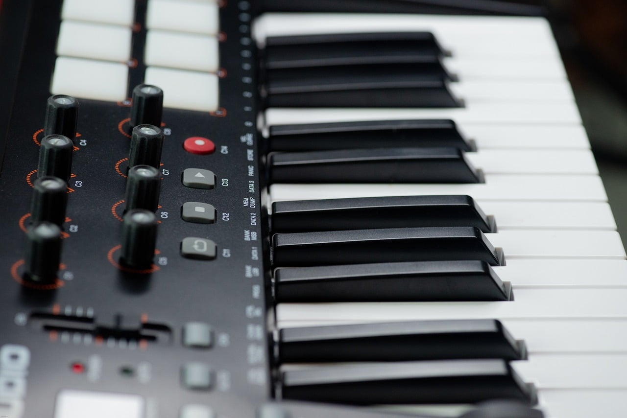 Close-up of a keyboard synthesizer focusing on the black and white keys with sliders and control buttons in the foreground.