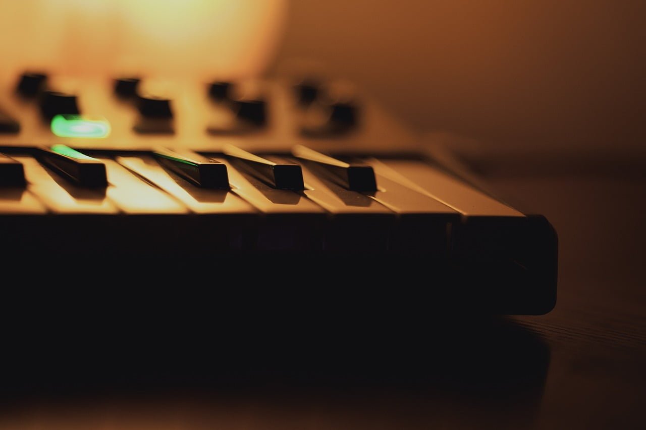 Close-up of a keyboard piano in a dimly lit room with a shallow depth of field, focusing on a few black keys with a warm ambient glow in the background.