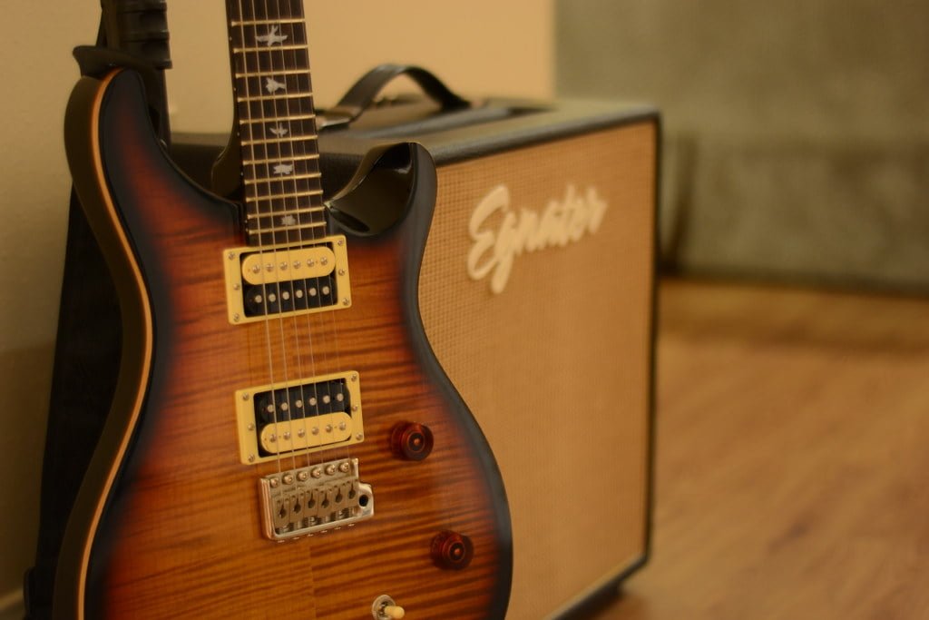 A close-up of an electric guitar with a sunburst finish leaning against a guitar amp with the brand name "Egnater" visible.