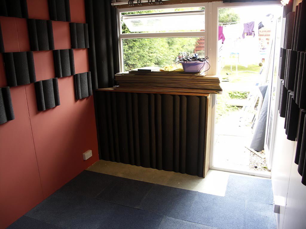 A recording studio with soundproof foam on the walls and a window overlooking a backyard with a clothesline.