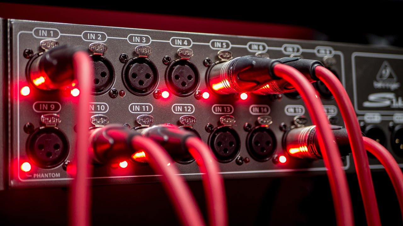 Close-up of an audio interface with red LED lights and connected red cables inserted into XLR input ports, labeled from IN 1 to IN 14.