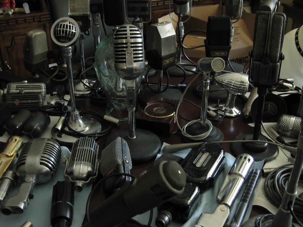 A collection of various vintage and modern microphones cluttered together on a surface.