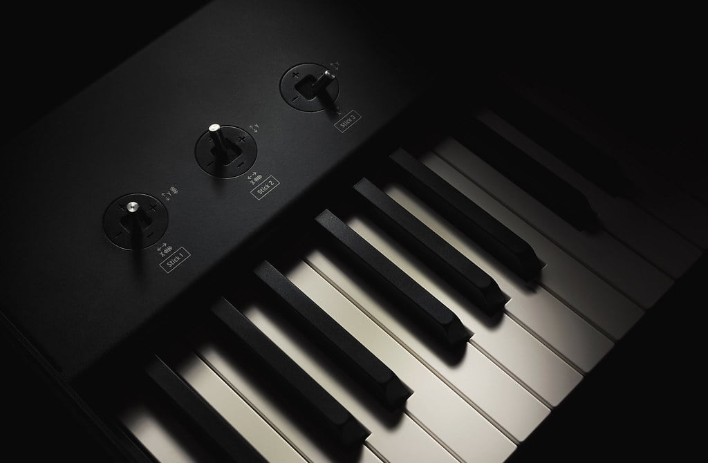 Close-up of a piano keyboard with focus on black and white keys, along with control knobs above the keys, set against a dark background.