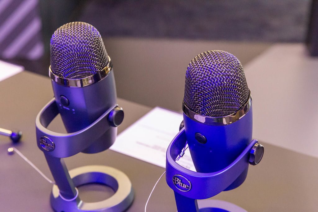 Two blue Yeti microphones on stands displayed on a table.