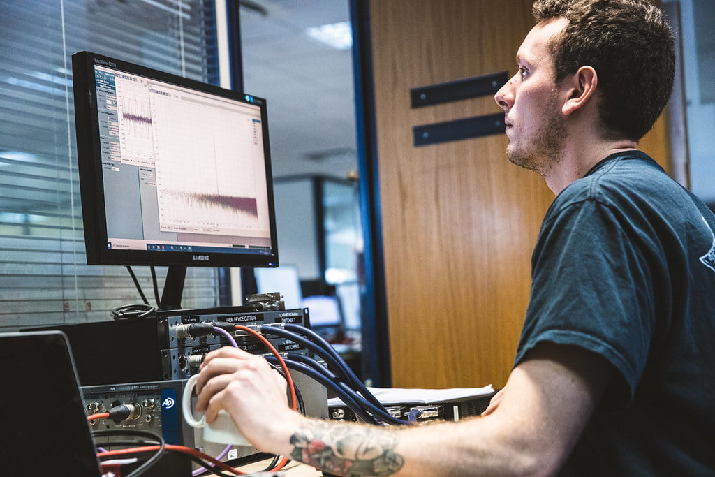 Man analyzing data on a computer monitor with graphs, while working with electronic equipment in an office setting.