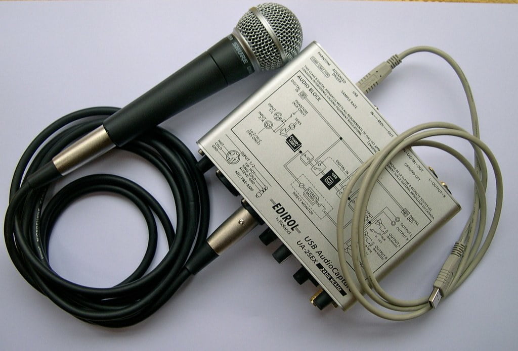 A handheld microphone with an XLR cable connected to an external USB audio interface, placed on a white surface.