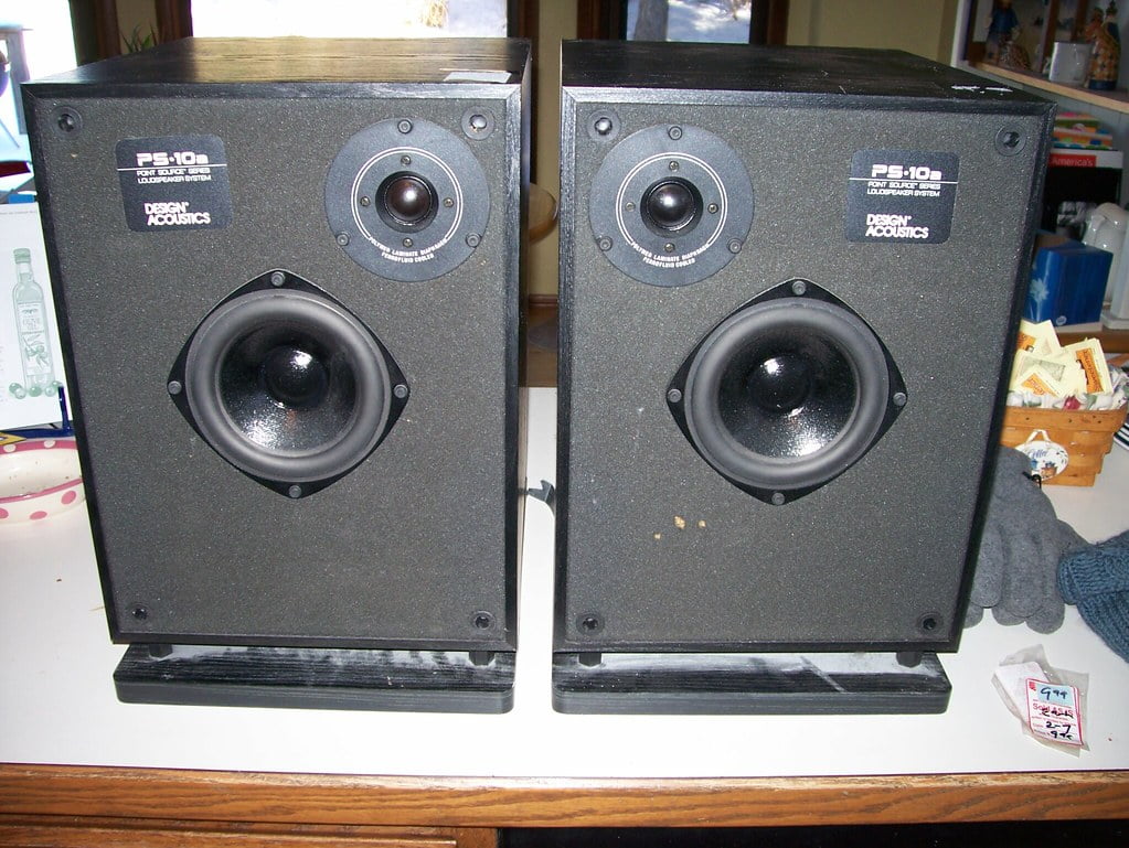 Two black Design Acoustics PS-10 bookshelf speakers on a wooden surface.