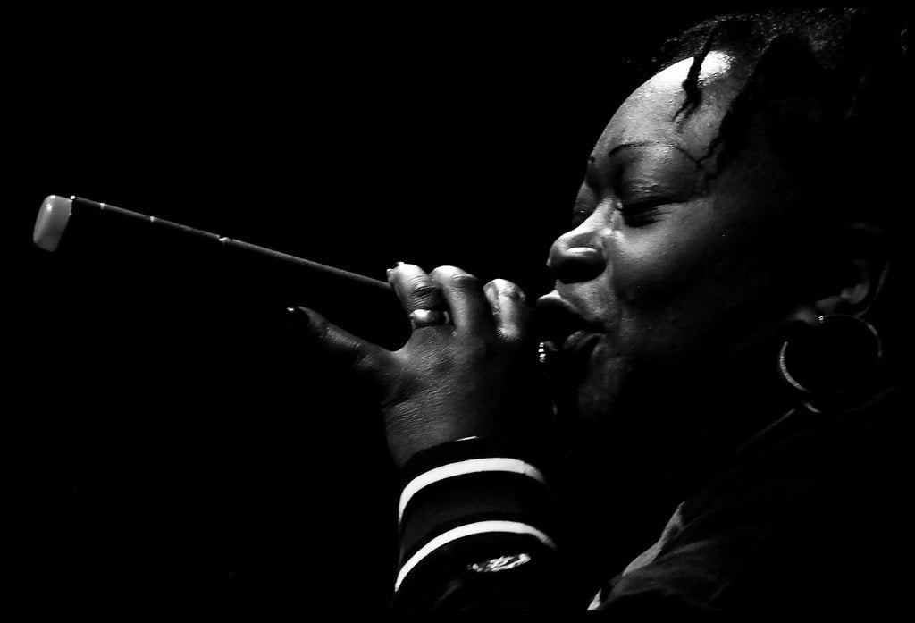 A black and white silhouette of a person singing into a microphone onstage.