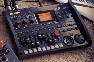 A Zoom R8 multi-track recorder and audio interface on a carpeted floor.