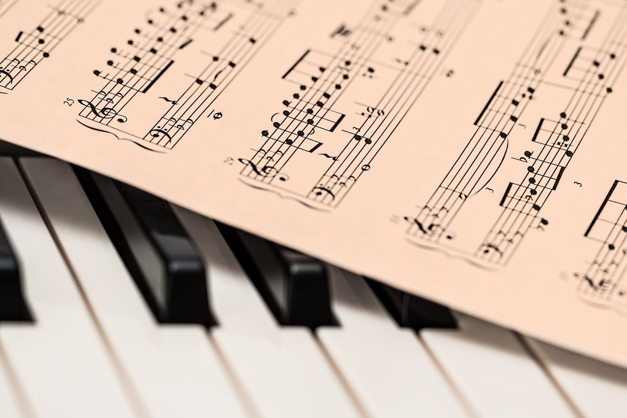 Sheet music on a stand with a shallow depth of field, above piano keys with the focus on the sheet music.