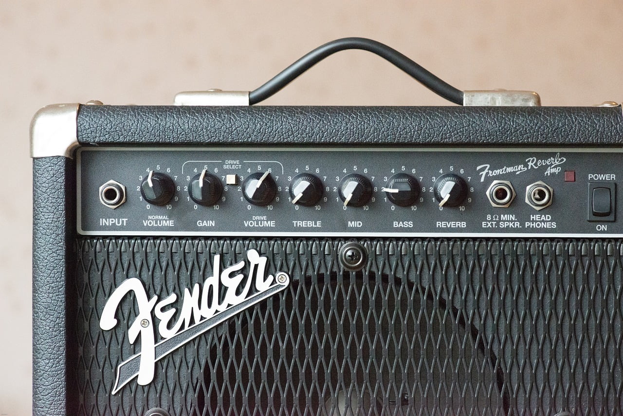 A close-up of a Fender Frontman Reverb guitar amplifier, displaying various control knobs for volume, gain, treble, mid, bass, and reverb, alongside input and output jacks.